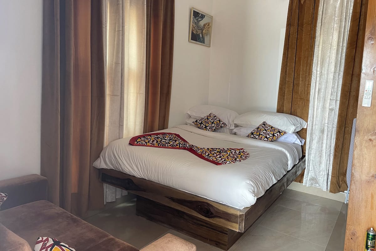 Quarto com estrutura de cama em madeira, roupa de cama branca e almofadas estampadas.