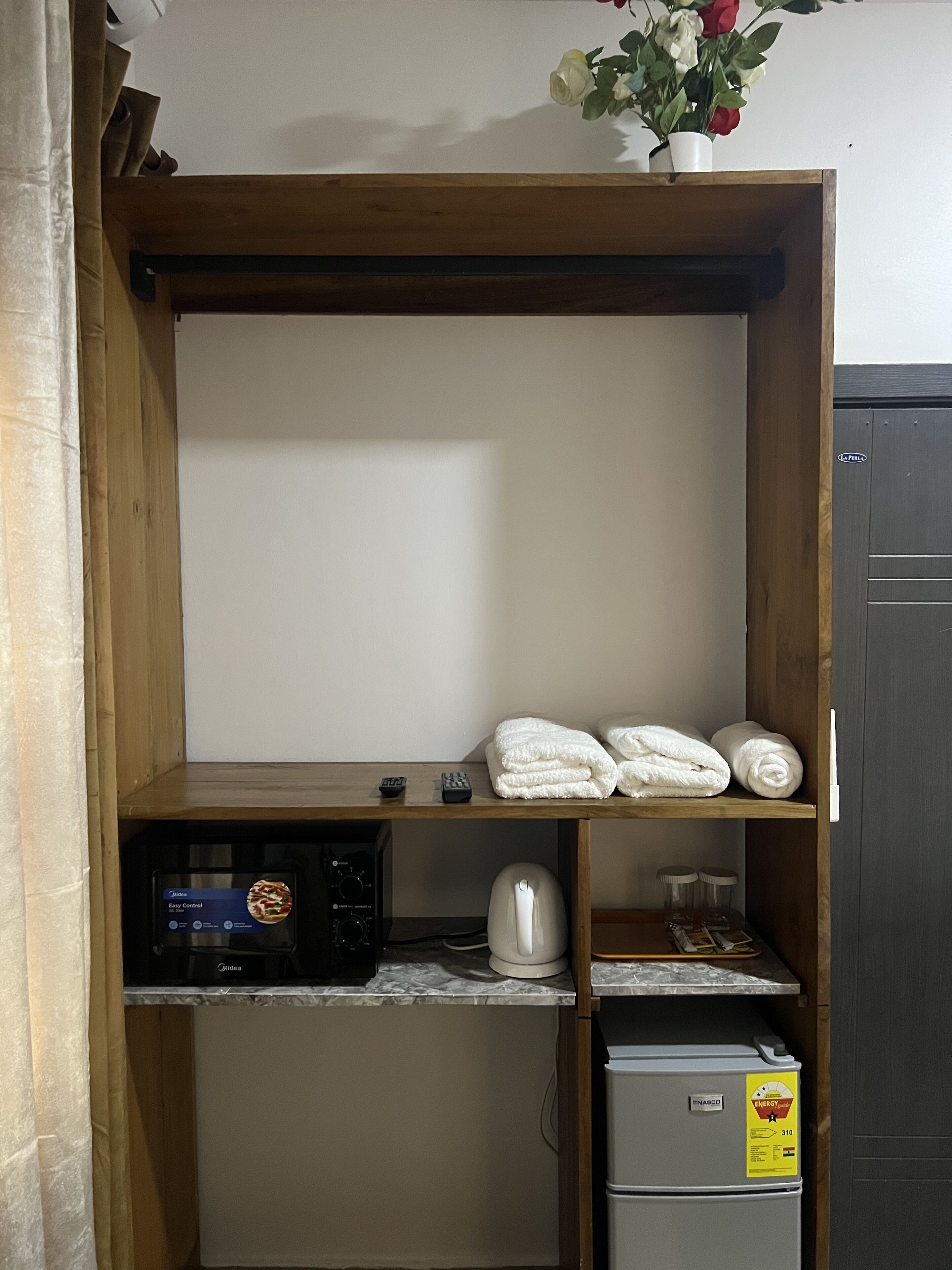 A wooden shelf unit with towels, a kettle, a coffee maker, and a refrigerator.