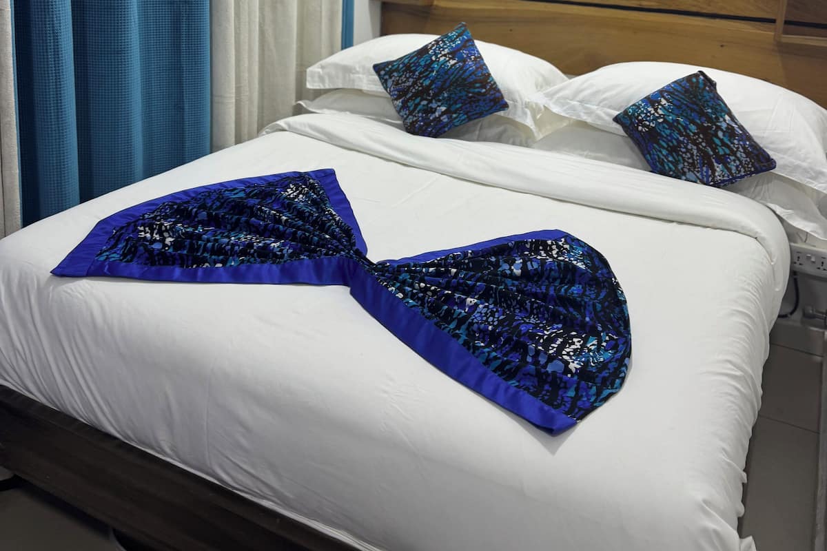 Cama bem arrumada com lençóis brancos e almofadas estampadas em azul, cabeceira de madeira e um quadro de flores na parede.