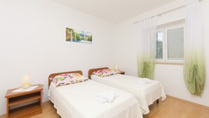 Ein Schlafzimmer mit zwei Einzelbetten, einem Nachttisch mit Lampe, einem Fenster mit Vorhängen und einem Wandbild.