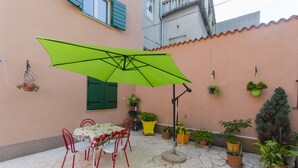 Eine Terrasse mit Tisch und Stühlen, einem grünen Sonnenschirm und Topfpflanzen.