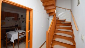 Eine Holztreppe mit Teppichstufen, ein Essbereich mit Tisch und Stühlen, und eine Küche, die durch eine offene Tür sichtbar ist.