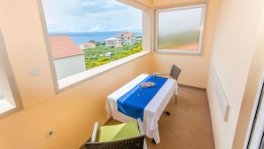 A balcony with a table set for two, a chair, and a view of the sea and buildings. - Apartments and Room Napoli (Bol)