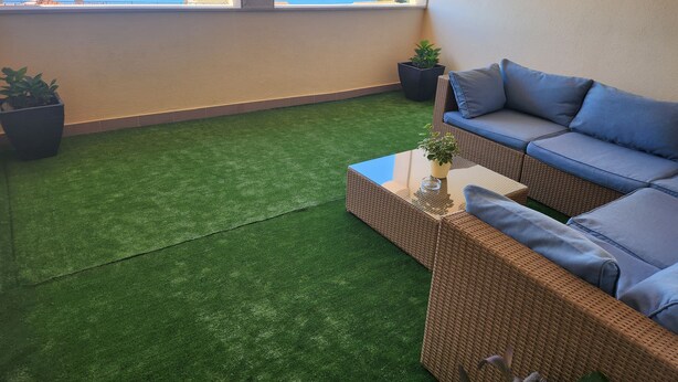 A balcony with artificial grass, a wicker sofa with blue cushions, and a view of the sea and mountains. - Apartments and Room Napoli (Bol)