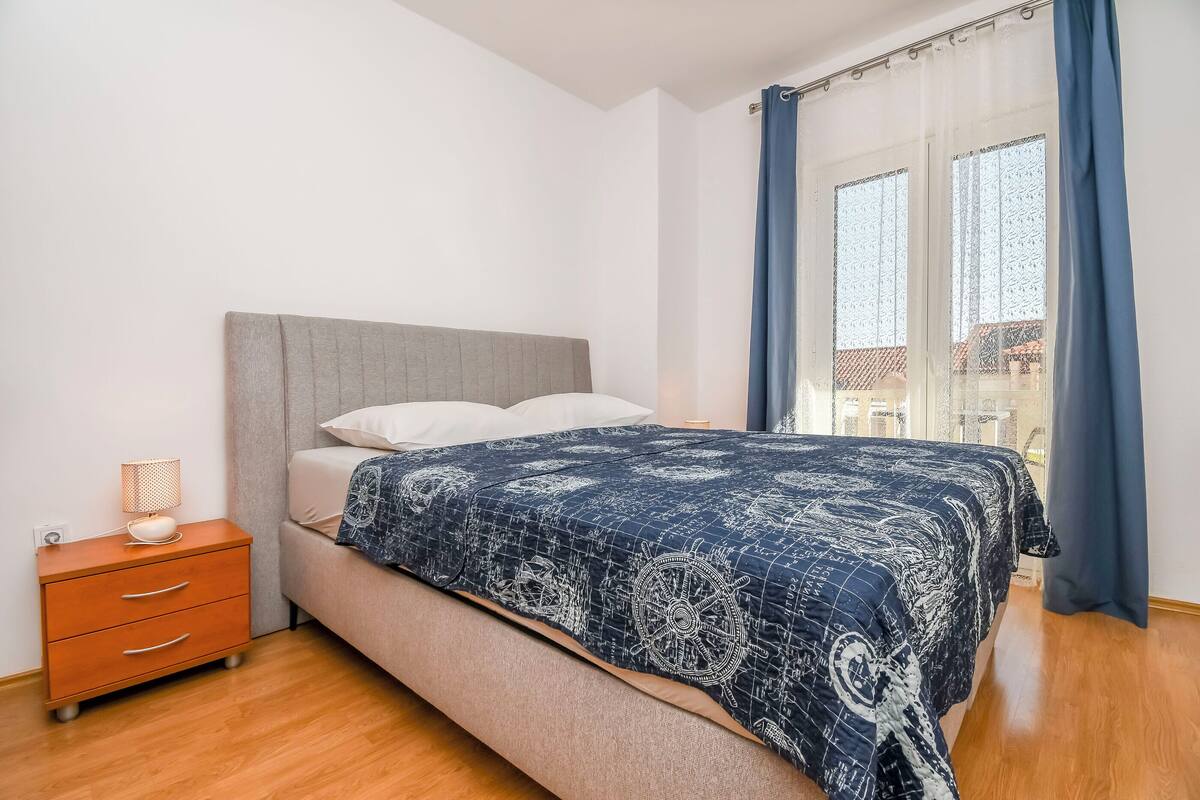 A bedroom with a bed, a nightstand, and a window with curtains.