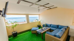 A balcony with a green artificial turf floor, a wicker sofa with blue cushions, a small table with a bottle and glasses, and a potted plant. - Apartments and Room Napoli (Bol)
