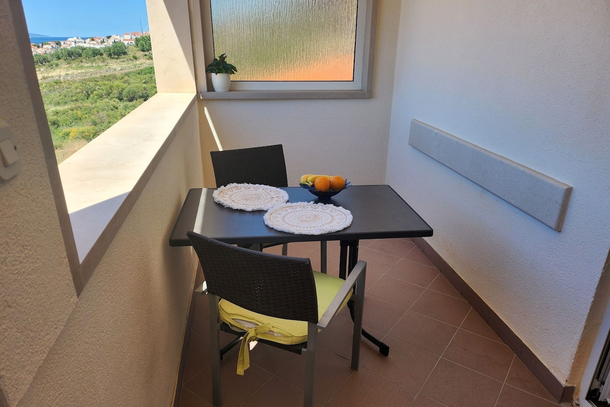 A small balcony with a table, two chairs, a bowl of fruit, and a potted plant.