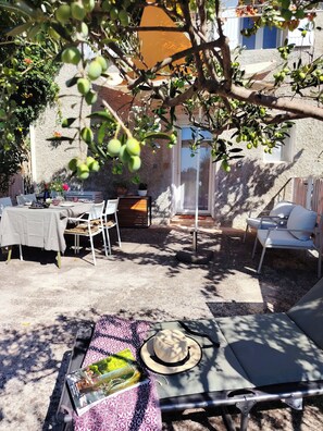 An outdoor patio with a table set for dining, surrounded by chairs, and a lounge area with a sunbed and a hat.