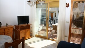 A room with a bed, a TV, a wooden cabinet, and a balcony with a table and chairs. - Adosado Peñisol Inmomart (Peñiscola)