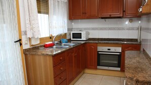 A kitchen with wooden cabinets, a microwave, an oven, and a sink. - Adosado Peñisol Inmomart (Peñiscola)