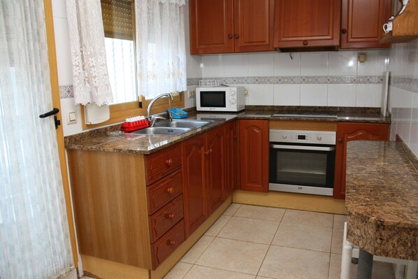 A kitchen with wooden cabinets, a microwave, an oven, and a sink.