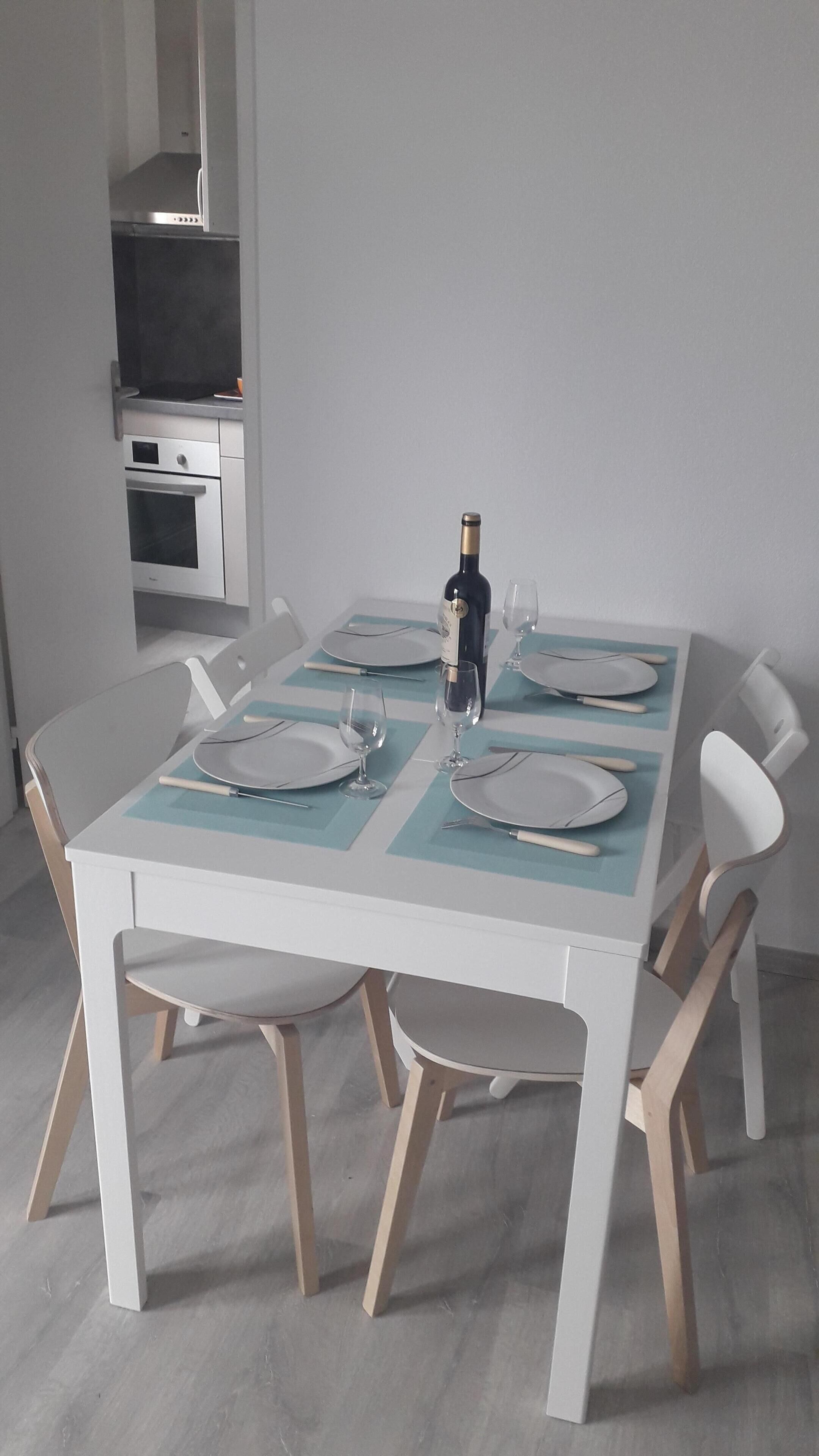 A dining table set for four with white chairs, a bottle of wine, and wine glasses.