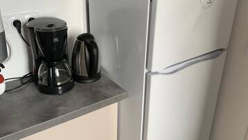 Pieni, käytännöllinen keittiö, jossa on mikroaaltouuni, kahvinkeitin ja vedenkeitin työtasolla.