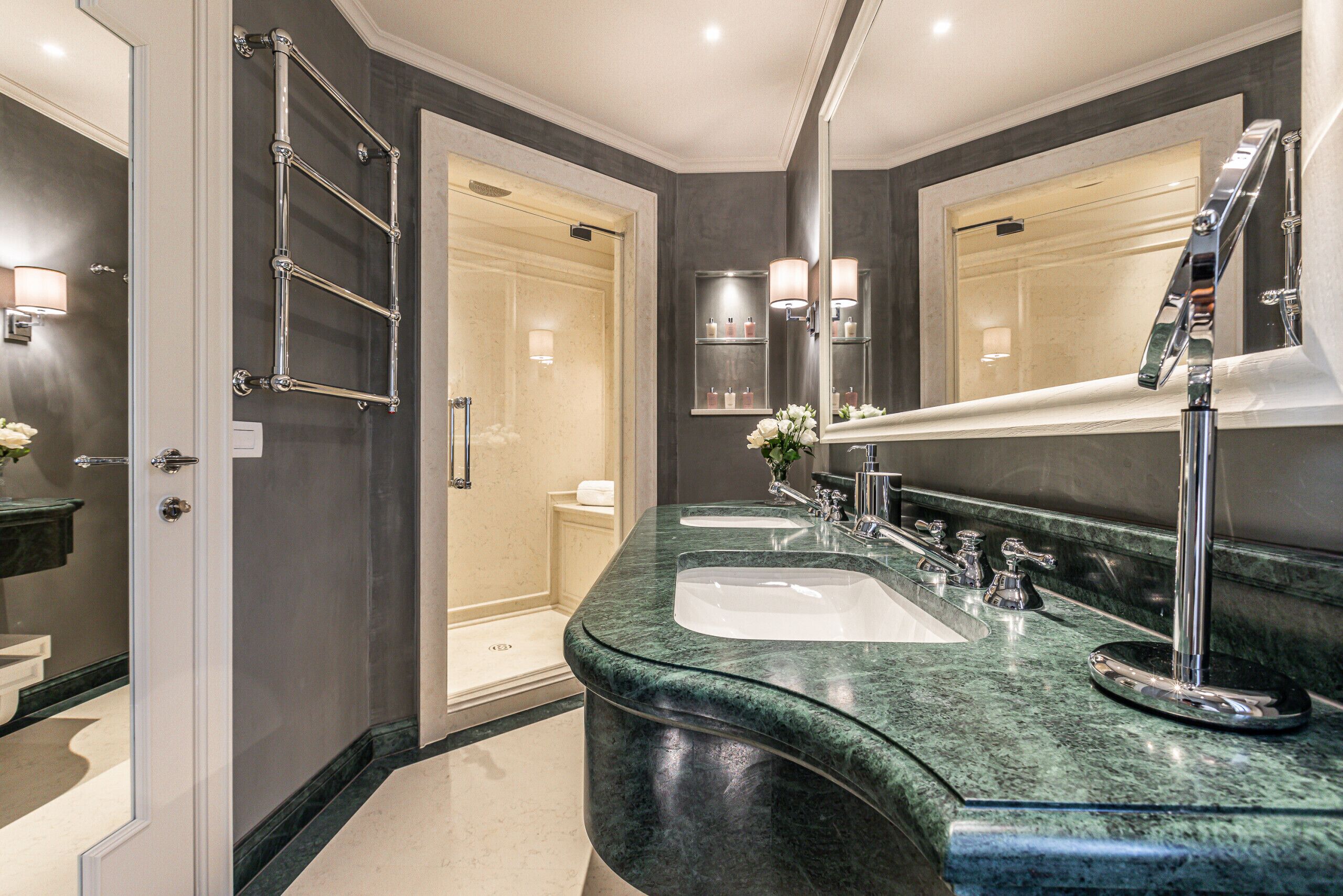 A modern bathroom with a curved granite countertop, two sinks, a large mirror, and a walk-in shower.