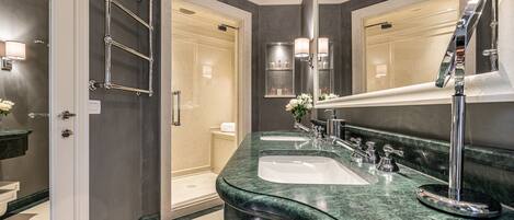 A modern bathroom with a curved granite countertop, two sinks, a large mirror, and a walk-in shower.