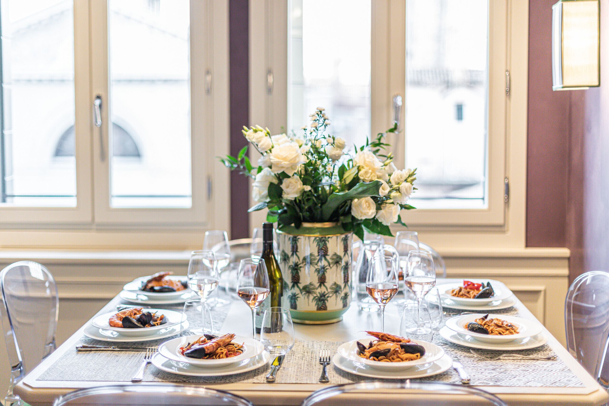 Une table à manger dressée avec des assiettes remplies de nourriture, des verres à vin et un vase de fleurs.