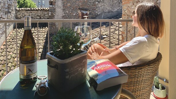 Ein Balkon mit einer Steinmauer, einer Weinflasche, einem Blumentopf und einem Buch.