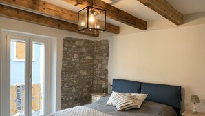 Ein Schlafzimmer mit einer Steinwand, einem Bett mit gesteppter Bettdecke, einem Nachttisch mit Lampe und einer Holzbalkendecke.