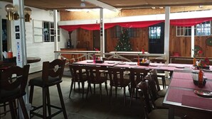 A restaurant with wooden walls, red curtains, and a Christmas tree. Tables are set with plates, glasses, and napkins. - Mlima View Gardens (Nanyuki)