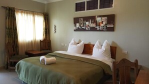 A hotel room with a bed, a chair, a small table, and a wall-mounted artwork. - Mlima View Gardens (Nanyuki)