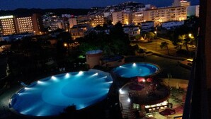 A nighttime view of a resort with two illuminated swimming pools, a landscaped area, and surrounding buildings. - Studio Rosas Spain (ROSES)