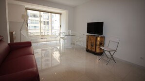 Ein modernes Wohnzimmer mit einem roten Sofa, einem Glastisch, einem Fernseher auf einer Anrichte und einem Balkon mit Blick auf Gebäude.