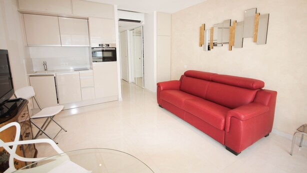 A modern living area with a red sofa, a glass coffee table, and a kitchen with white cabinets. - Modern Studio 1 minute from La Croisette (Cannes)