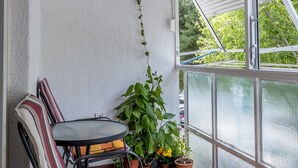 A balcony with a table and chairs, potted plants, and a view through a screened window. - Apartment Gordana (ST) - One Bedroom Apartment (Split)