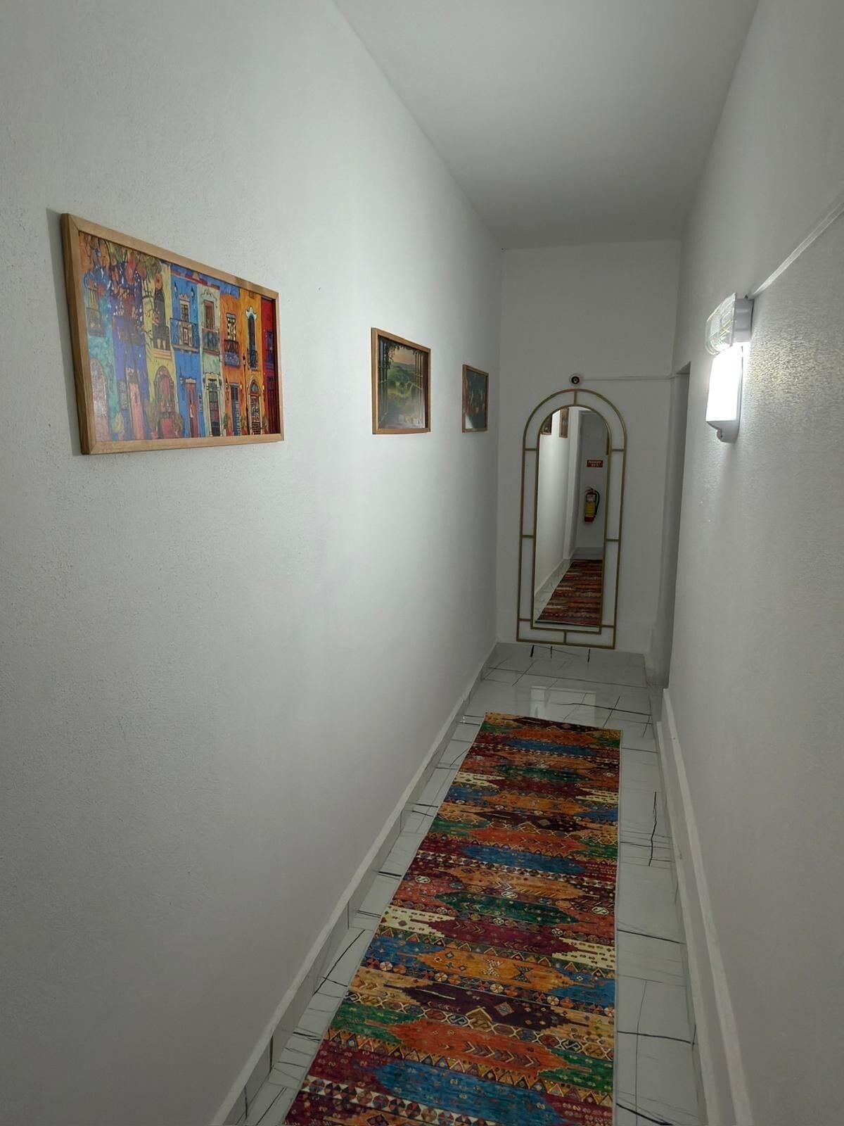 A hallway with white walls, a colorful patterned rug, and three framed artworks.
