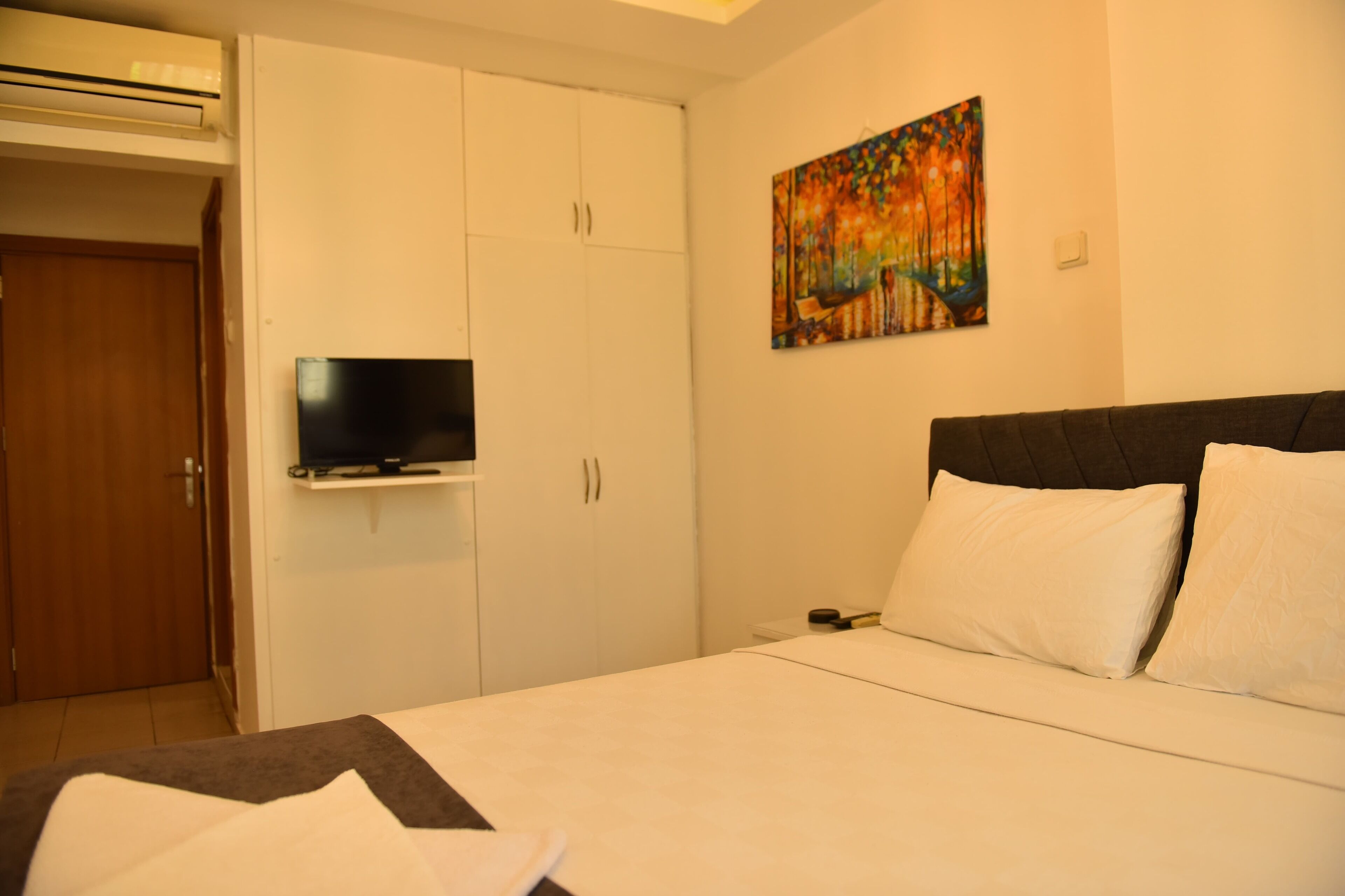 A hotel room with a bed, a television mounted on the wall, and a painting above the bed.