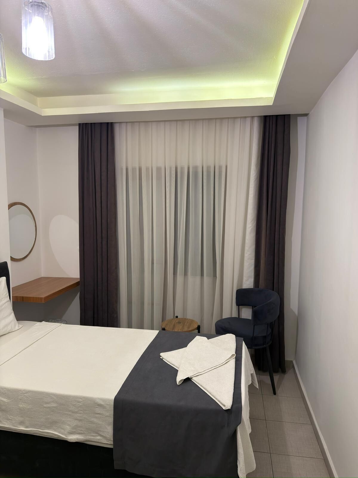 Ein Hotelzimmer mit Bett, Stuhl, kleinem Tisch und einem fenster mit Vorhängen.