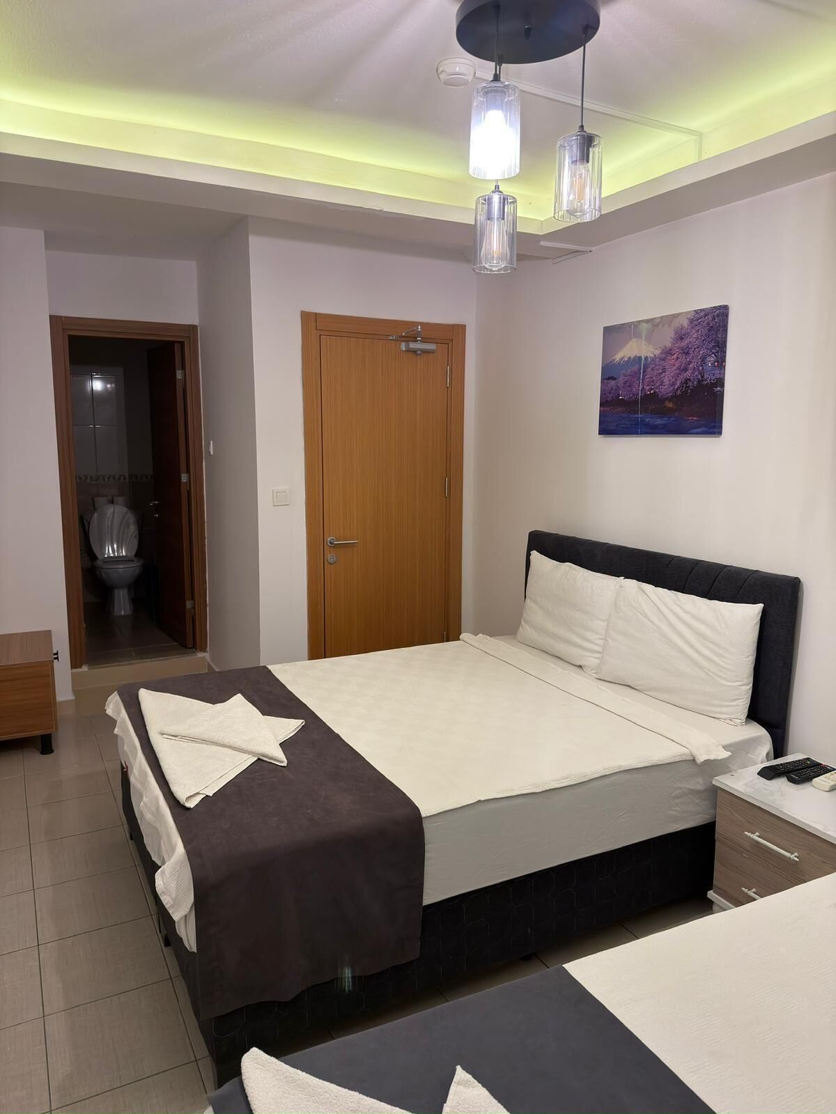 A bedroom with a bed, bedside tables, a door, and a painting on the wall.