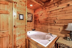 Interior de una cabaña de madera con una puerta de madera, un certificado enmarcado en la pared y una bañera blanca con un banco de madera.