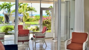 Ein Zimmer mit Glastür, das auf einen Balkon mit Korbmöbeln und Blick auf das Meer und grüne Vegetation führt.