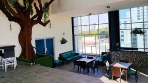 A modern interior with a large tree sculpture, green seating, and large windows offering views of the city.