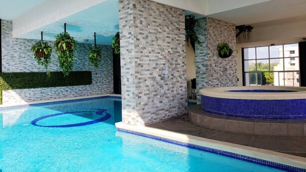 A swimming pool with a tiled edge, a hot tub area, and hanging plants.