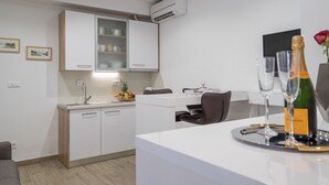 Una cuina moderna amb armaris blancs, un vàter integrat i una zona de menjador amb taula i caires blancs. Hi ha una ampolla de xampany i gots sobre la taula.
