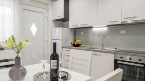 Una cuina moderna amb armaris blancs, un forn d'acer inoxidable i un plat de fruita al taulell.