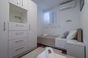 A compact bedroom with a bed, a bedside table, a wardrobe, and an air conditioning unit. - Drop In Split Suites (Split)