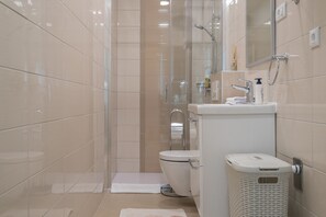 A modern bathroom with a glass shower enclosure, a white sink with a mirror, and a white toilet. - Drop In Split Suites (Split)