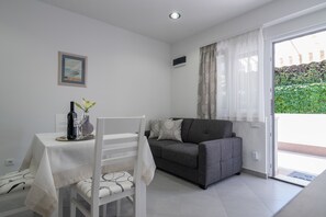 A modern living room with a dining table, a sofa, and a large window with curtains. - Drop In Split Suites (Split)