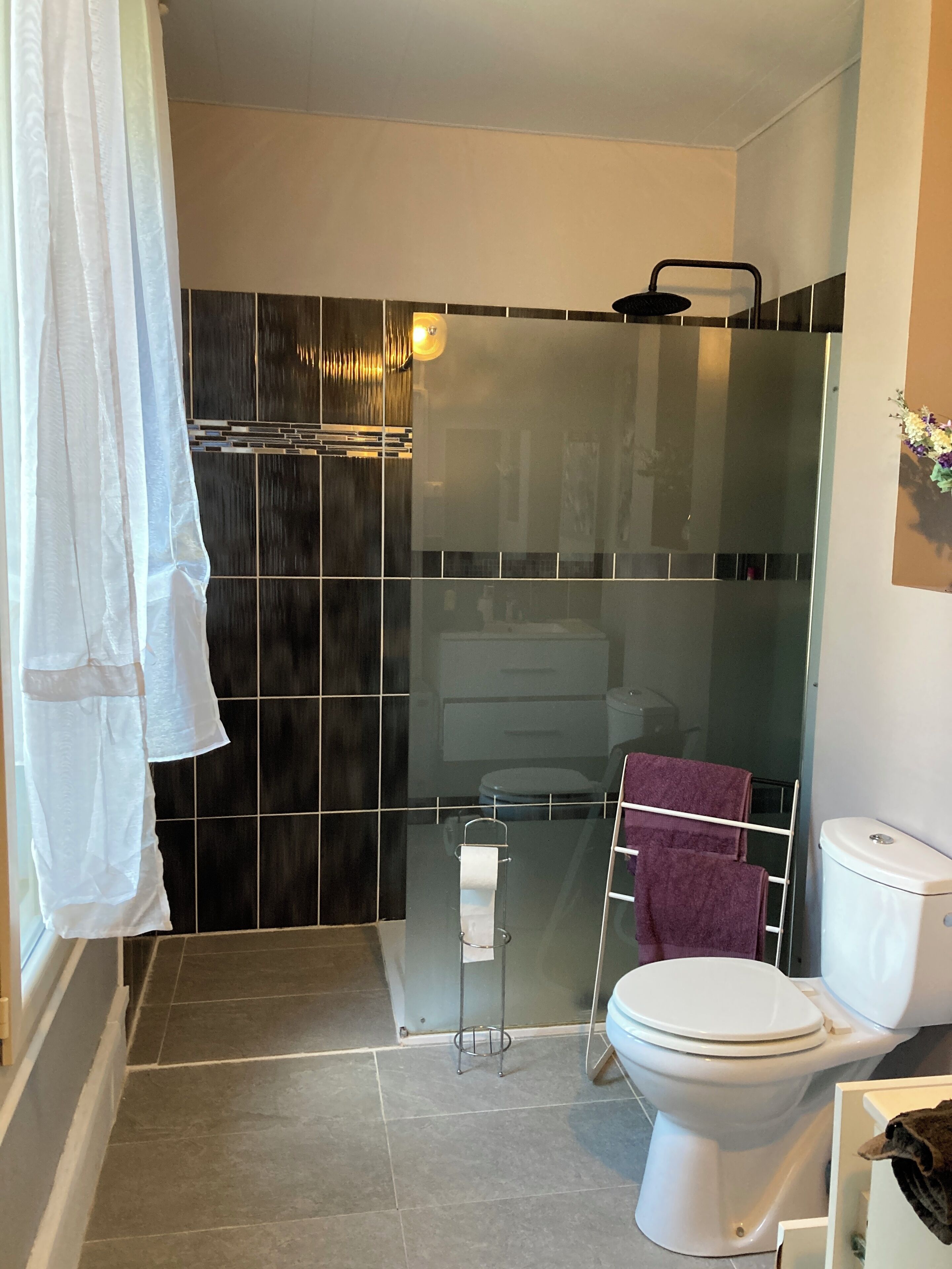 Een moderne badkamer met een douchecabine van glas, een wit toilet en een handdoekhouder met een paarse handdoek.