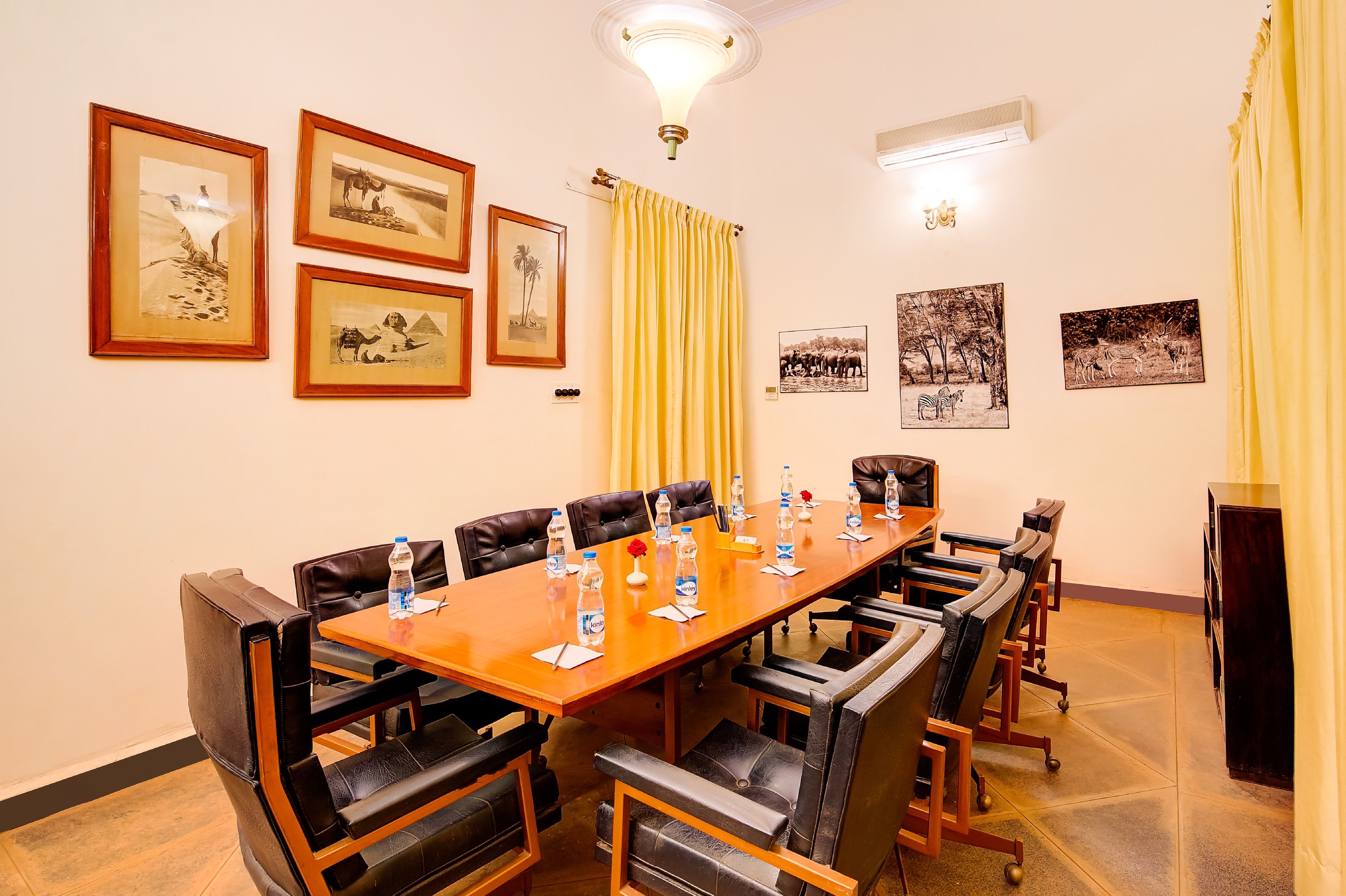 Un salón de conferencias con una larga mesa, sillas de cuero, cuadros en la pared y una cortina amarilla.