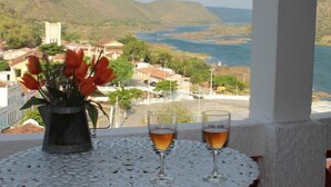 Varanda com uma mesa, dois copos de bebida e um vaso de flores vermelhas.