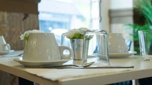 Uma mesa posta com xícaras e pires brancos, um copo e uma colher.