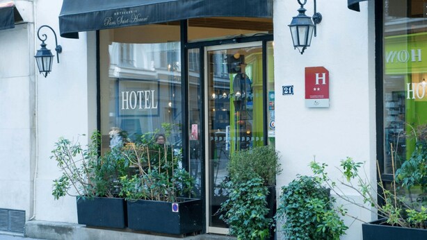 Entrada de hotel com porta de vidro, placa indicando o quarto 21 e pequena placa com um 'H' vermelho e estrelas.