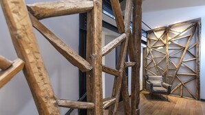 Um quarto com design geométrico na parede de madeira, uma escada de madeira e uma cadeira.