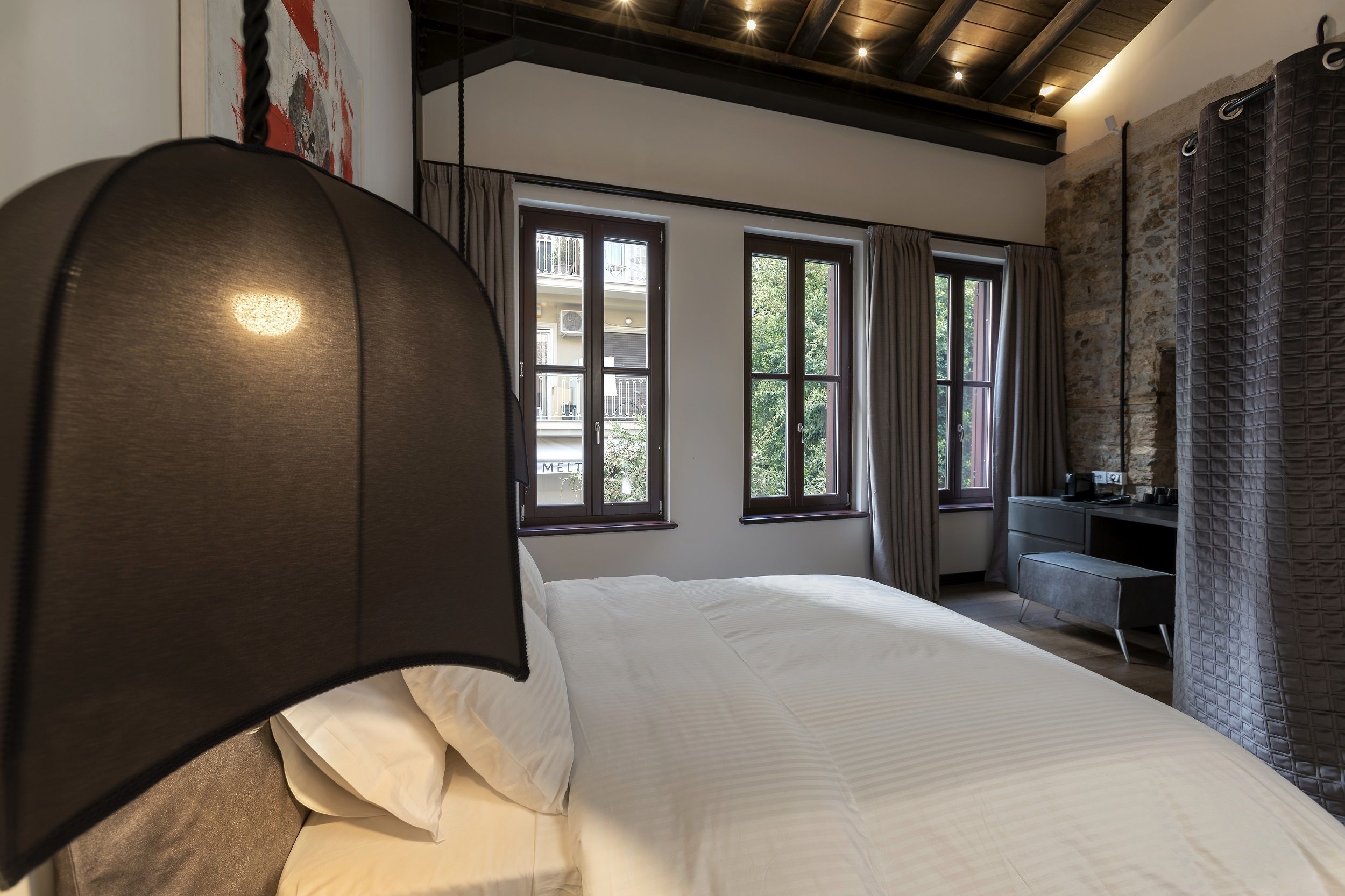 Quarto com uma cama grande, uma escrivaninha e vista para o exterior pelas janelas.
