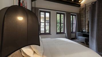Quarto com uma cama grande, uma escrivaninha e vista para o exterior pelas janelas.