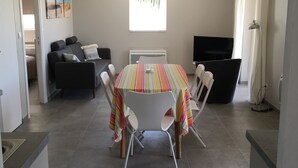 Un salon moderne avec un coin repas, comprenant une grande fenêtre, un canapé, un téléviseur et une table à manger avec des chaises.